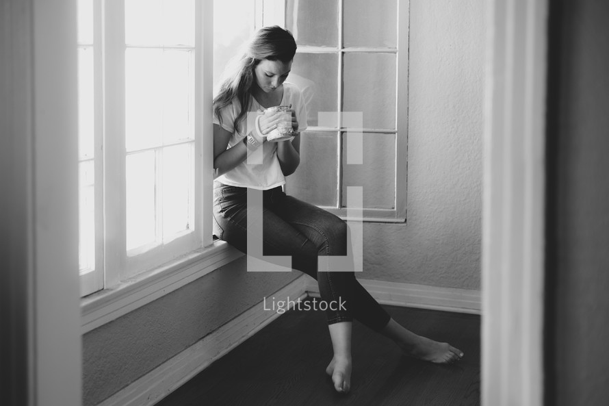 woman sitting in a window sill holding a cup of coffee 