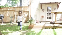 A little boy runs joyfully through the back yard into the arms of his father.