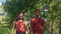 Young positive latin couple walking holding hands date in summer city park. Man and woman enjoying spend time together