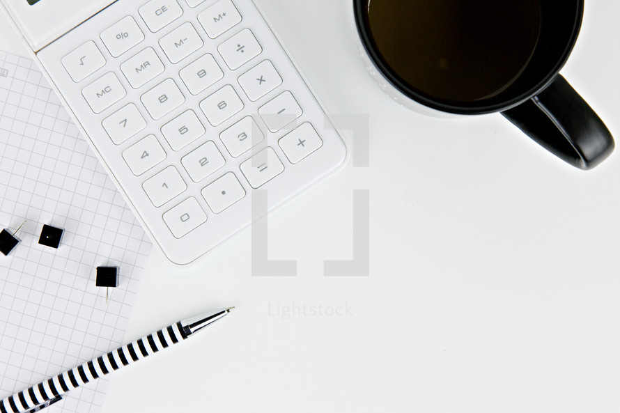 coffee mug, graph paper, pen, and calculator on a white desk 