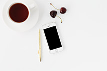 coffee cup, pen, cherries, and iPhone on a white background 