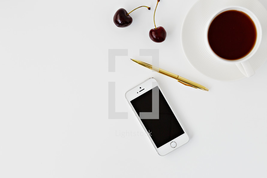 iPhone, gold pen, cherries, and coffee on white 