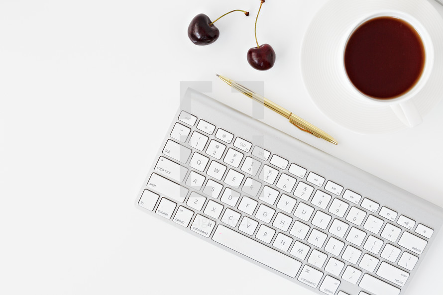 computer keyboard, gold pen, cherries, and cup of tea 