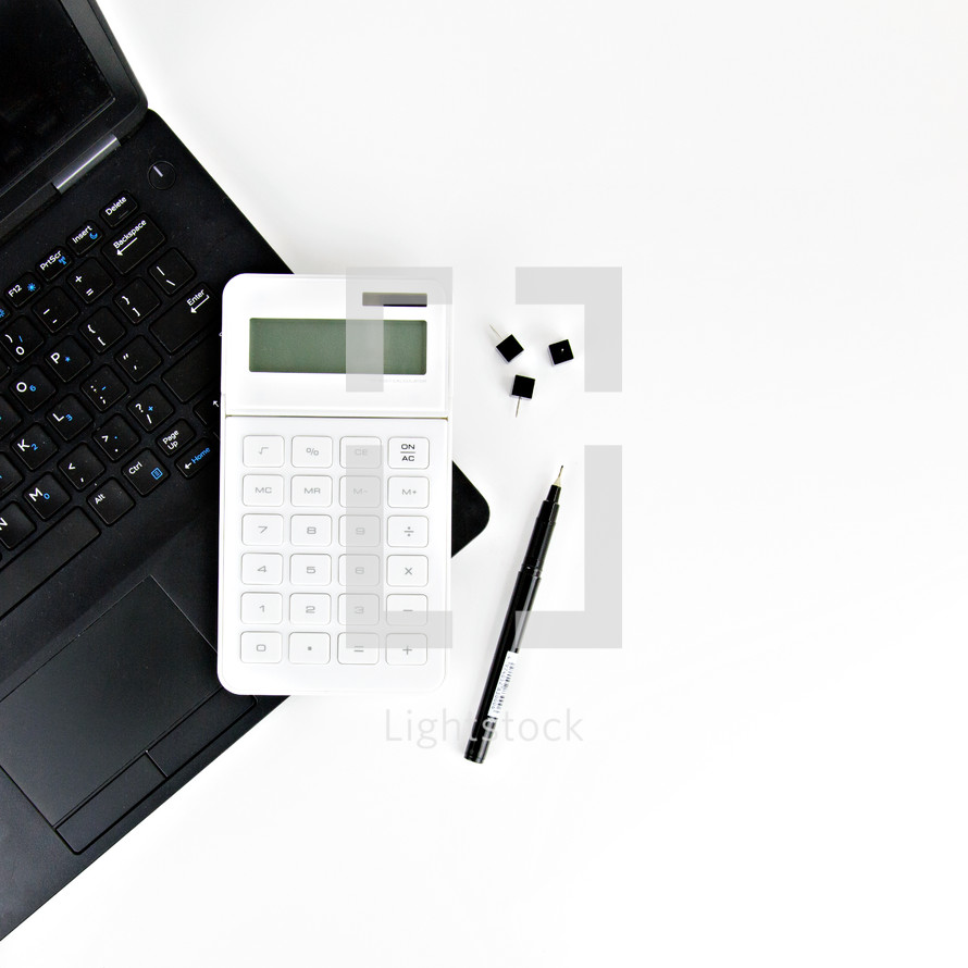 tacks, pen, laptop computer, and calculator on a desk 
