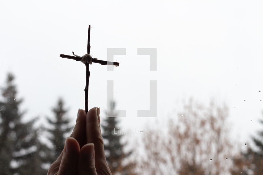 praying hands holding up a cross made of sticks 