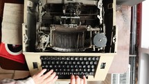 Overhead view of a person typing on an antique manual typewriter.