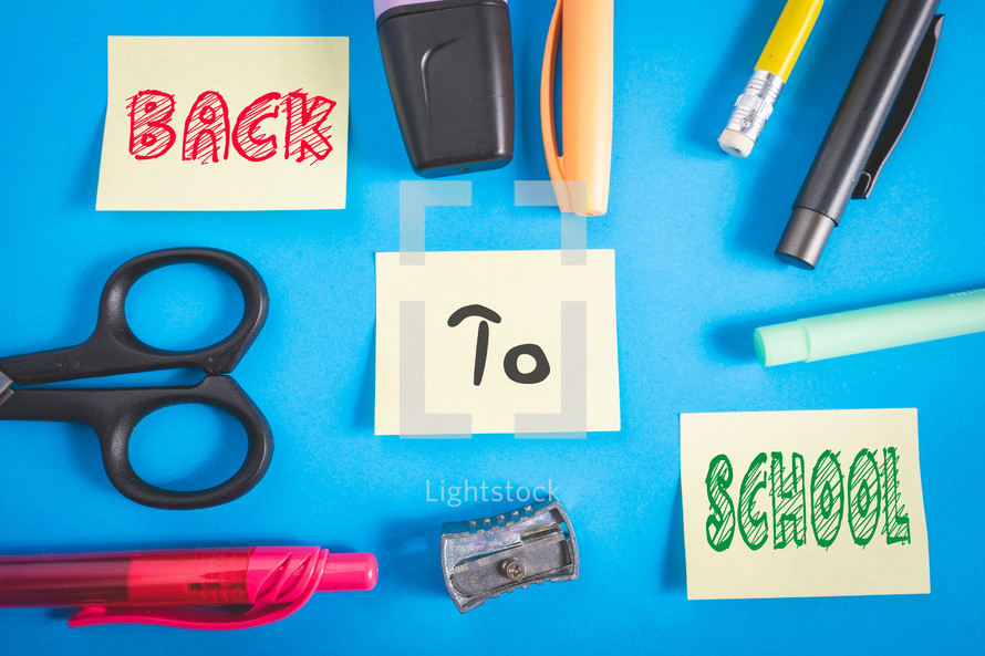 Office and school supplies on a blue background. And three sticky notes with back to school on it.