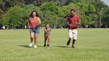 Cute latino boy and his parents are playing in the park. Family have fun running during a weekend in nature.

