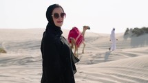 Portrait of Muslim woman at the desert with camelleers leading camel behind
