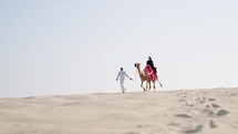 Tourist woman riding camel with cameleer leading
