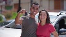 Young hispanic couple hugging each other holding key of new car at street
