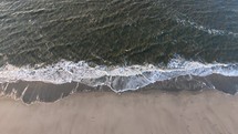 Aerial, static, drone shot of calm waves hitting a beach, on Langeoog island, on a sunny day, in North Germany