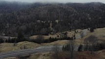 Aerial drone scenic view of a mountain road with dense trees against an overcast sky.
