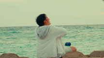 Asian man is sitting in front of the ocean and enjoying
