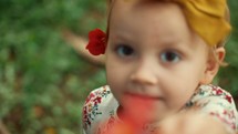 a happy toddler girl showing a flower to the camera 