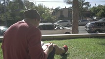 man sitting in grass reading a Bible on campus 