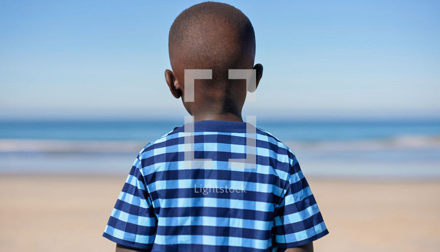 boy standing on a beach with back to camera