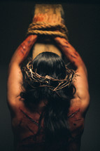 The suffering of Christ -- a beaten and scarred Jesus in His crown of thorns, bound to the cross with ropes.