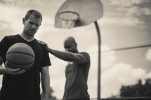 Men praying on a basketball court while holding a basketball.