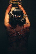 The suffering of Christ -- a beaten and scarred Jesus in His crown of thorns, bound to the cross with ropes.