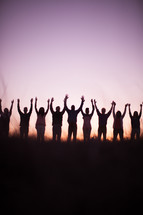 silhouette of people in a row outdoors with raised hands in praise 