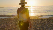 Tracking shot of a young woman walking on the beach during sunset