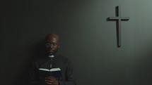 African American Priest Praying to God with Bible in Modern Church