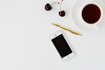 iPhone, gold pen, cherries, and coffee on white 