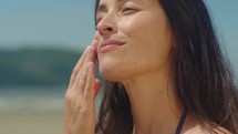 Close-up woman on bikini takes sunscreen of tube, moisturizing lotion applies sunblock on her face