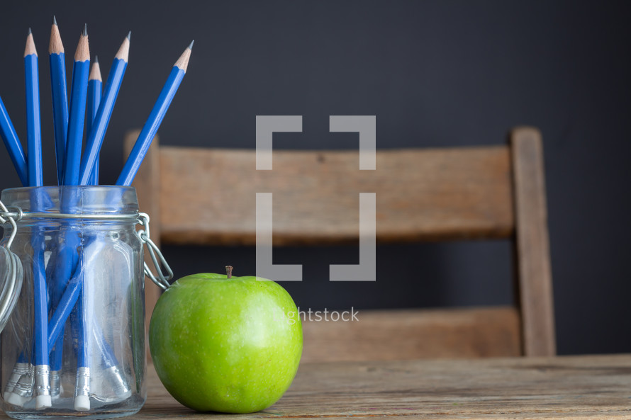 pencils in a jar and apple on a desk 