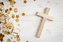 Gold confetti and streamers with a small wood cross on a white background with copy space