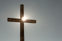 Sun shining on brown rustic wooden cross against sky