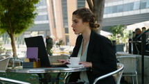 Young business woman sitting in a cafe working on a laptop computer and drinking coffee