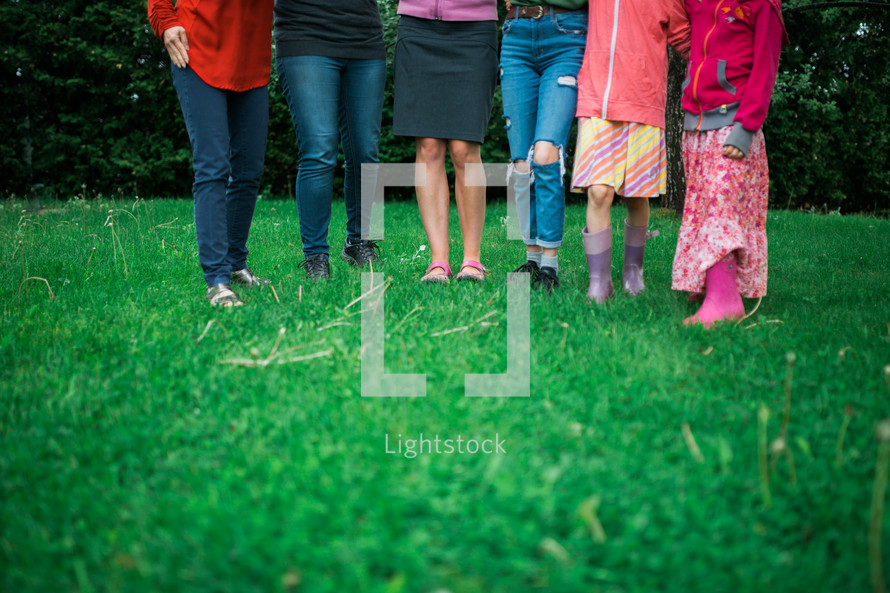 legs of females standing outdoors in grass 