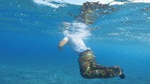 man with military trousers swims in the sea
