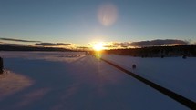 Aerial of an orange sunset and a highway running through snow country