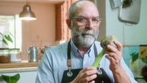 Senior food blogger showing artichoke and describing it on camera, giving online cooking class or filming video recipe in the kitchen. Tilt-up shot
