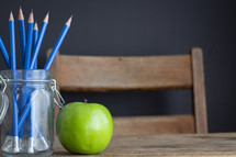 pencils in a jar and apple on a desk 