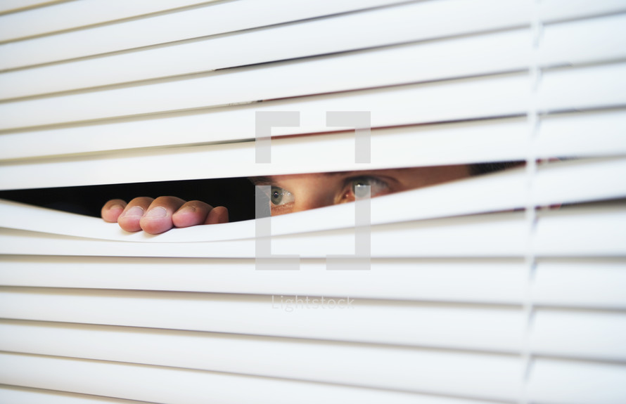 Caucasian man looking through the slats of a blind