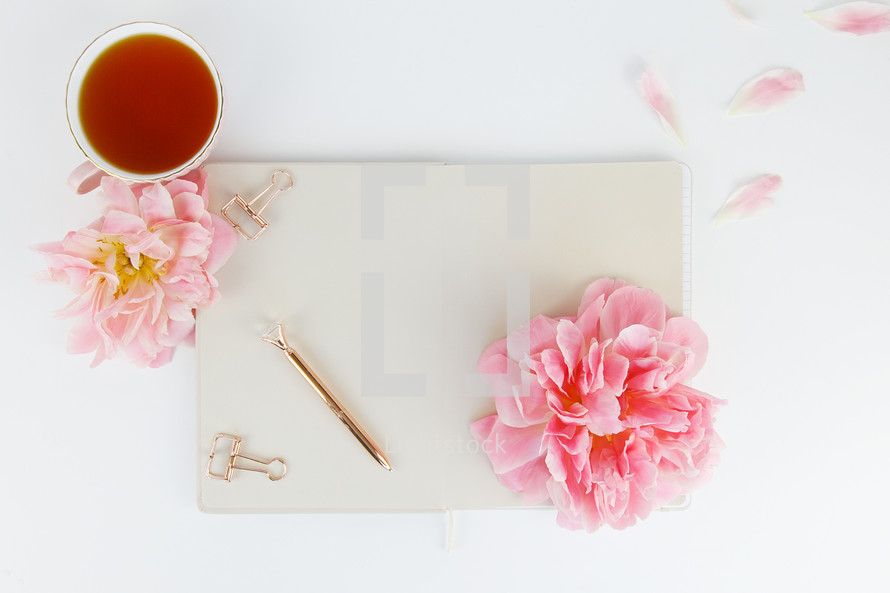 tea cup, notepad, pen, clips, and pink flowers on a desk 