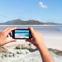 person taking a picture at a beach with a cellphone 