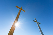 Sunlight on two wooden Christian crosses against blue sky
