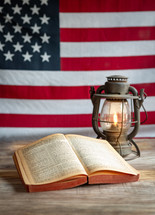 Open Holy Bible and old fashioned oil lamp with American flag background vertical