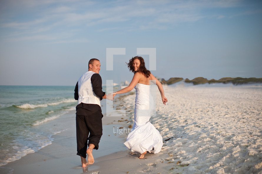 bride and groom holding hands and running on a beach