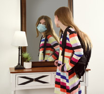 a student wearing a face mask looking in the mirror 
