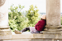 a little girl resting outdoors between columns 
