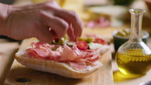 Hand of female chef putting thin slice of prosciutto on ciabatta bread while making gourmet sandwich. Close-up view, selective focus
