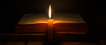 Bibles on a dark background lit up by a candle