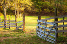 Open wooden and metal gate at entrance to grass field in rural setting 
