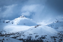 Snow covered mountain peak landscape with evergreen trees and dark clouds in Arapaho National Forest, Colorado